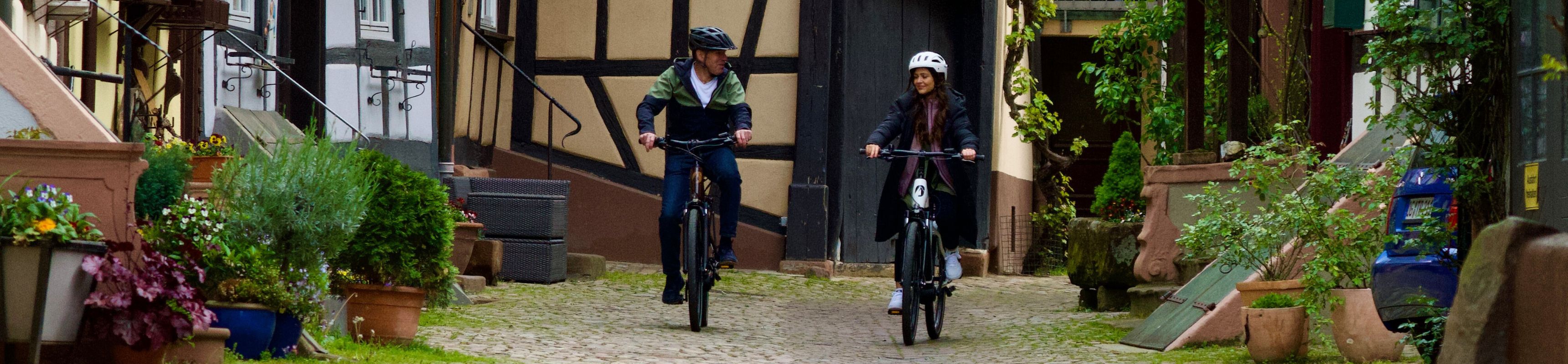 Zwei Radfahrer die mit ihren LIQBikes durch die Gengenbacher Innenstadt vor Fachwerkhäuser fahren